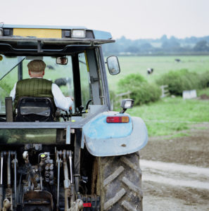 Senior male farmer driving tractor, rear view